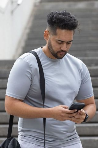 African american man checking smartphone on concrete stairs with gym bag and smartwatch