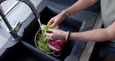 Woman washing fresh lettuce and radicchio at kitchen sink