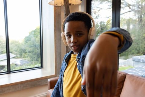 African american boy wearing headphones in sunlit living room, denim jacket