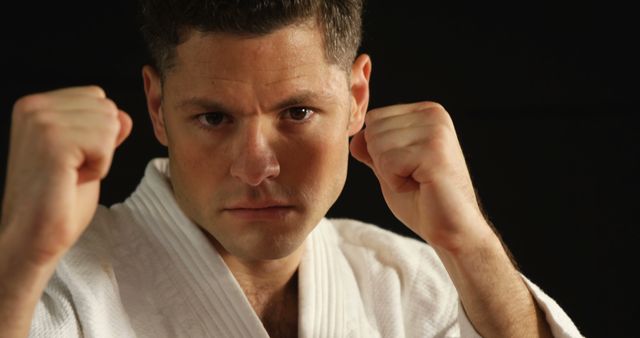 Focused martial artist holds hands in fighting stance wearing a white gi. Ideal for articles on martial arts, training techniques, self-defense classes, and personal discipline. Can also be used in promotional materials for martial arts schools or fitness programs.