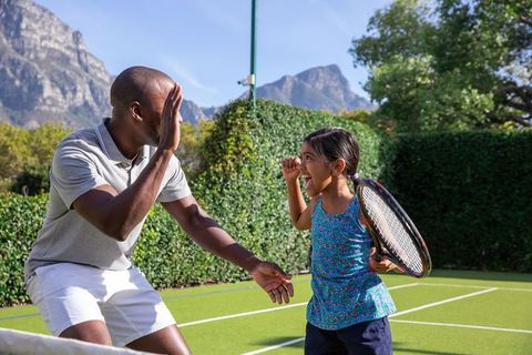 Father and daughter high-five during tennis practice outdoors