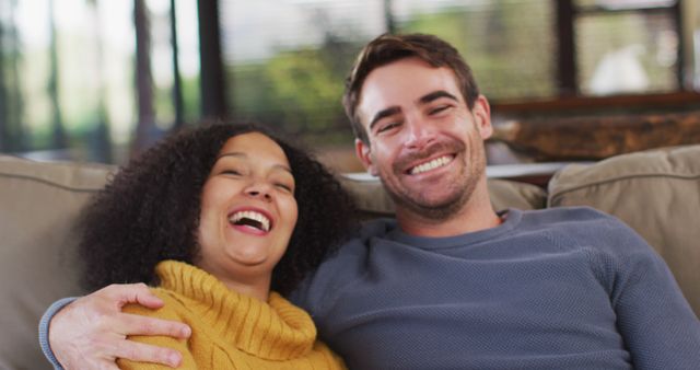 Portrait of happy diverse couple sitting on couch in living room, embracing and smiling. spending free time together at home.