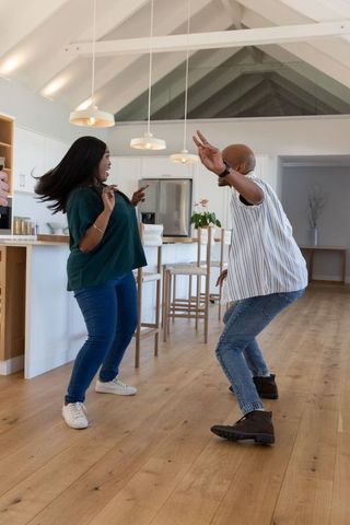 Asian woman and african american man dancing playfully in modern open-plan kitchen
