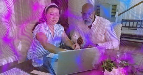 Senior and adult daughter collaborating at home laptop with purple wavy digital overlay