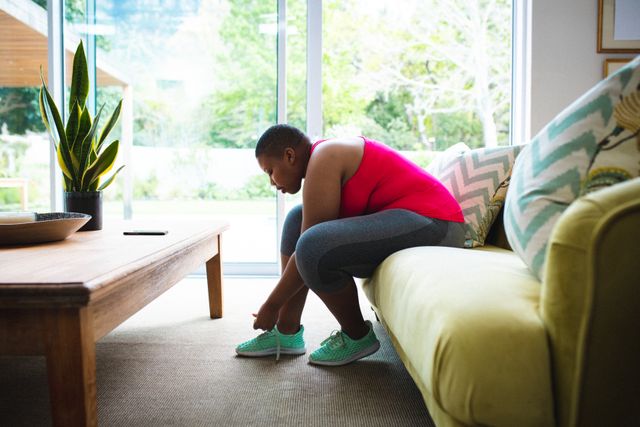 African american woman tying her shoelaces while sitting on the couch at home. fitness and healthy lifestyle concept