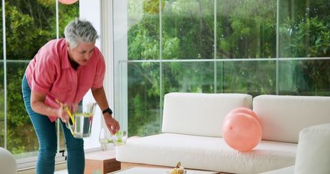Senior Woman Cleaning Living Room After Birthday Party with Balloons