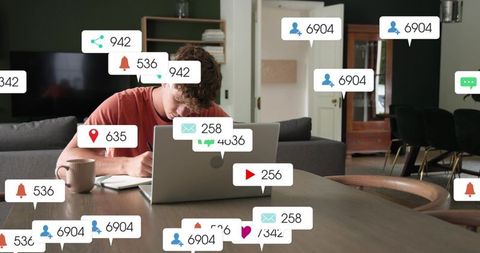 Young man writing in notebook at laptop with floating notification icons, remote work focus