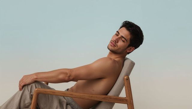 Shirtless man reclining on lounge chair, leaning back, pastel gradient studio backdrop