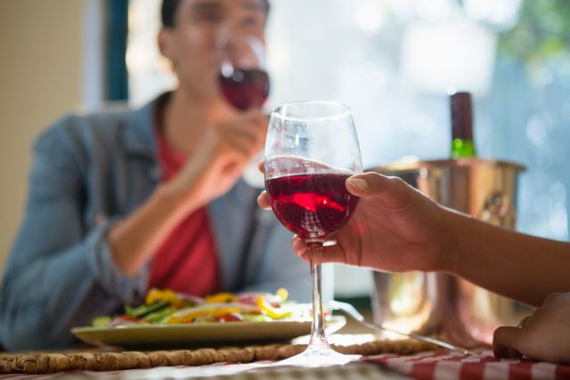 Cropped hand of woman with friend holding wineglass at table in restaurant