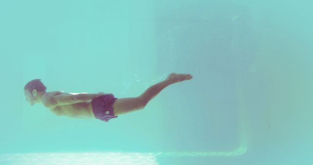 Man swimming underwater in clear blue pool. Useful for advertisements related to fitness, swimming, summer activities, athletic training programs, or leisure.