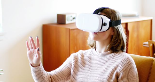 Woman wearing VR headset, engaging with virtual content in a living room. Potential use in articles or ads related to home VR experiences, technological advancements, virtual reality products, and immersive interactive entertainment at home.
