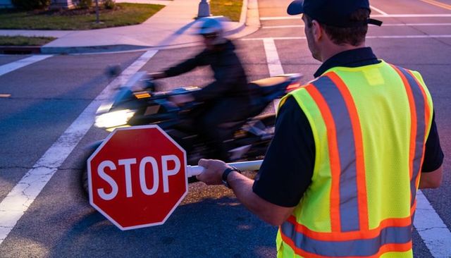 Flagger holding stop sign controlling suburban traffic at dusk with motorcyclist passing