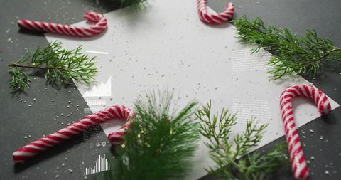 Festive flatlay featuring blank white paper, candy canes, pine sprigs and snow on dark tabletop