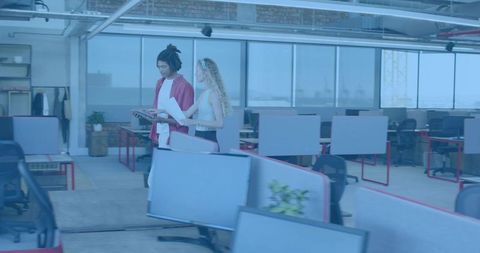 Coworkers walking and collaborating in open-plan office holding tablet and documents