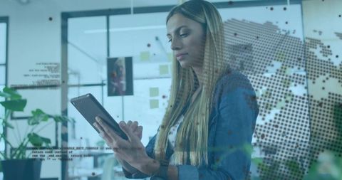 Businesswoman analyzing global data on tablet with dotted world map overlay in office