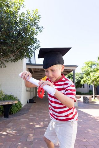 Young boy celebrating graduation holding diploma and wearing mortarboard on campus