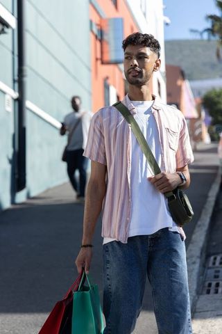 Asian man walking on colorful urban street carrying shopping bags in casual street style