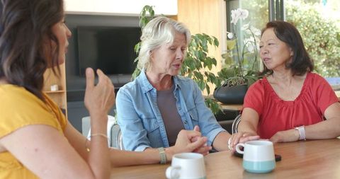 Diverse women holding hands sharing conversation over coffee at sunlit kitchen table