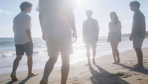 Friends walking on sunlit beach with backlit silhouettes, footprints and lens flare