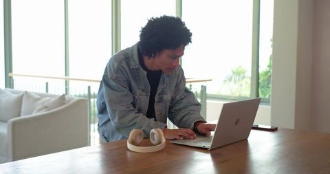 African American man leaning over laptop working from home in modern living room