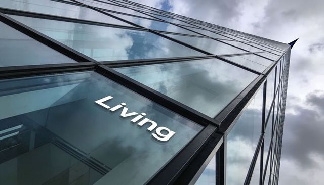 Glass facade skyscraper reflecting cloudy sky with living sign at sharp apex