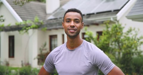 Young Man Standing Proudly in Front of Eco-friendly Home with Solar Panels