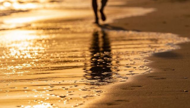 Silhouette walking along golden shoreline at sunset with footprints and sand reflections