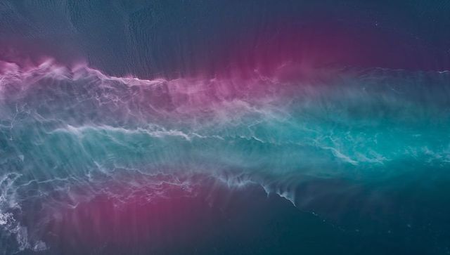 Aerial turquoise magenta wave band flowing with foamy crest and gradient ocean motion