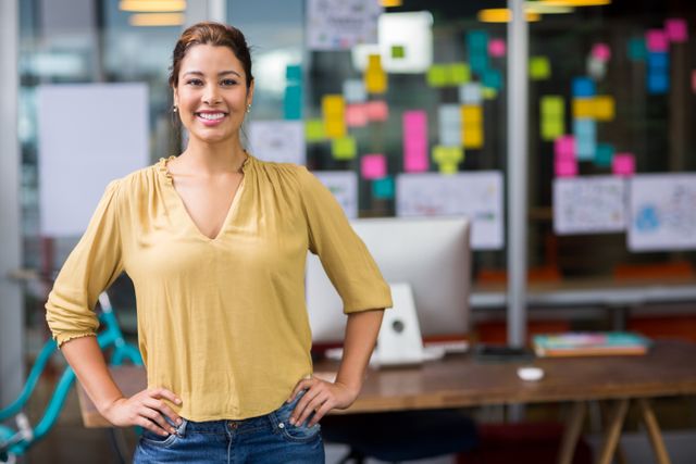 Portrait of smiling female executive standing with hands on hip at office