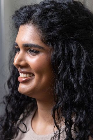Indian woman smiling in close-up headshot with curly hair, dimple and warm soft light