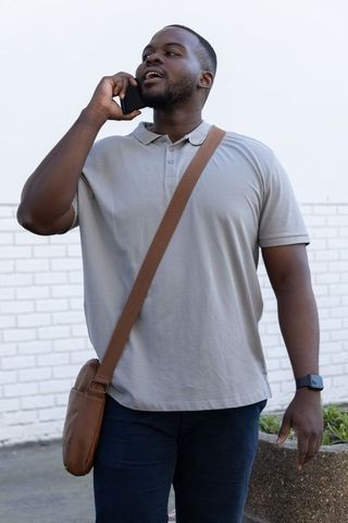 African American man walking and talking on phone with leather crossbody bag