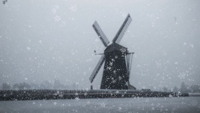 Windmill silhouetting in falling snow over canal, foggy winter monochrome landscape