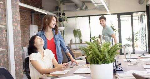 Smiling coworkers collaborating around desk with large potted fern in modern office