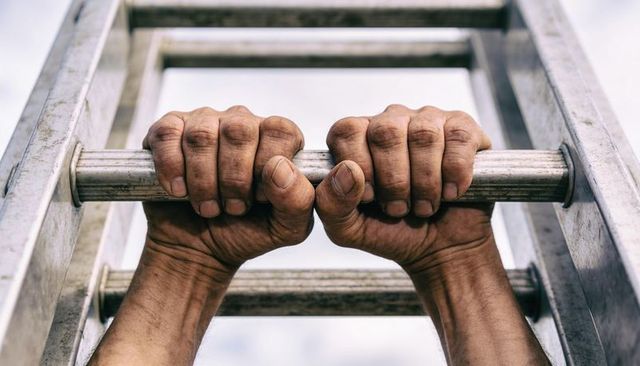 Gripping weathered hands holding metal ladder rung outdoors closeup of calloused palms