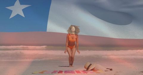 Sunlit beach fashion woman in orange swimsuit posing with straw hat and flag overlay