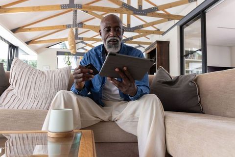 Senior african american man using tablet and credit card on sofa for online banking