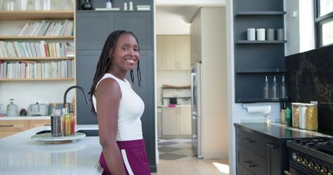 Smiling african woman leaning on kitchen island in modern minimalist bright home