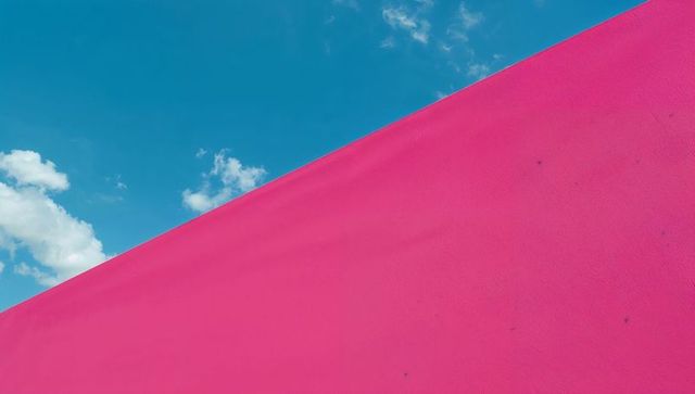 Hot pink diagonal colorblock against vibrant cyan sky with clouds minimalist geometric