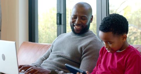 Smiling African American Father and Son Using Laptop and Tablet for Remote Learning