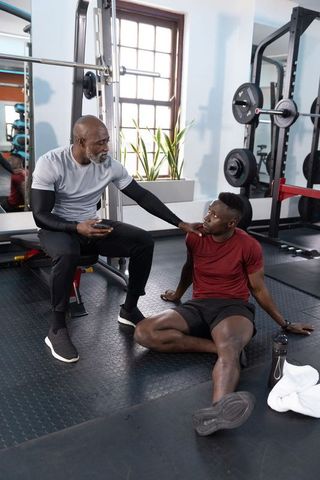 African american trainer guiding exhausted male trainee post-workout in modern gym