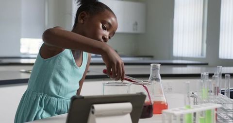 Young african girl conducting science experiment in school lab with tablet and beakers