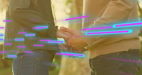 Couple holding hands at golden hour with neon light streaks, romantic outdoor connection