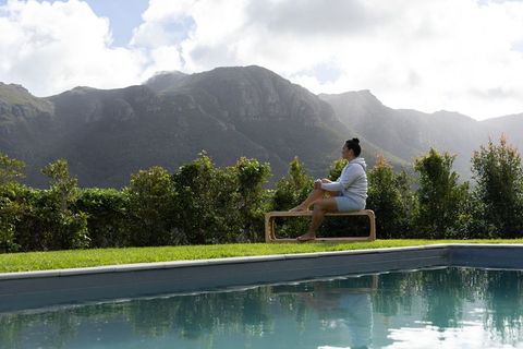 Asian woman relaxing by pool with serene mountain view holding mug on wooden bench