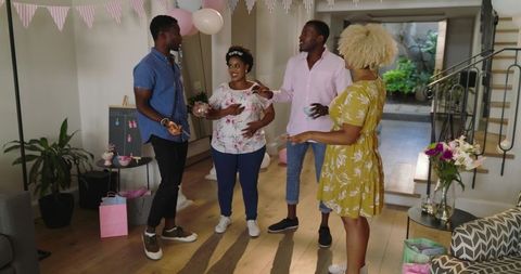 Diverse friends celebrating baby shower at home with pregnant woman wearing tiara and gifts