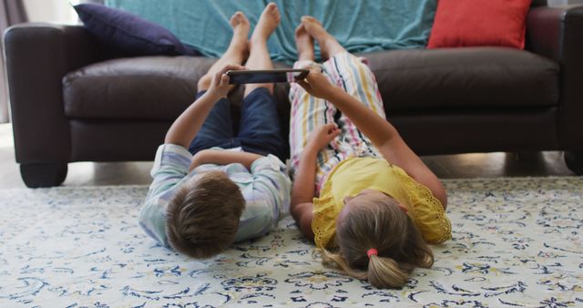 Happy caucasian brother and sister at home, lying on floor in living room using tablet together. happy family, free time at home.