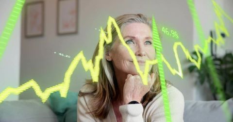 Mature woman contemplating finances with neon stock graphs overlay in modern living room
