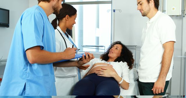 Pregnant woman lying on hospital bed, receiving consultation from medical staff including nurse and doctor. Her partner stands by her side, supporting her during hospital visit. Ideal for use in healthcare and maternity related contexts, promoting healthcare services, prenatal care, and family support during pregnancy.