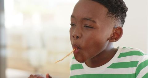 African american boy eating long spaghetti noodle playfully at home dining table