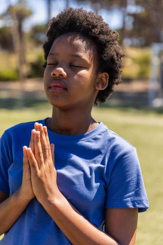 African american teen girl meditating outdoors with hands pressed in blue t-shirt