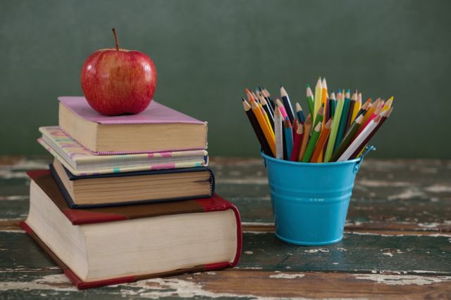 Close-up of apple on stack of books with pen holder